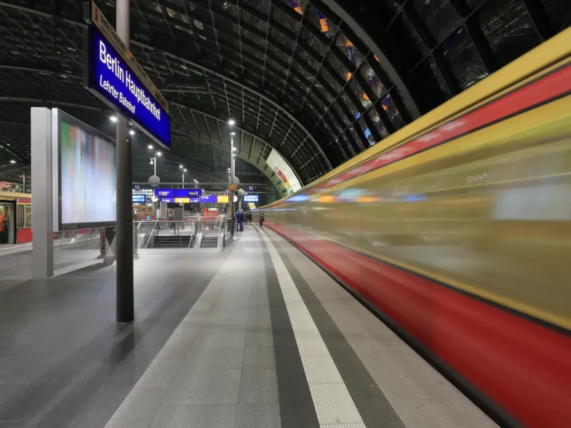 An S-Bahn train blurring through the upper platform at Berlin Hauptbahnhof beneath the station's name board.
