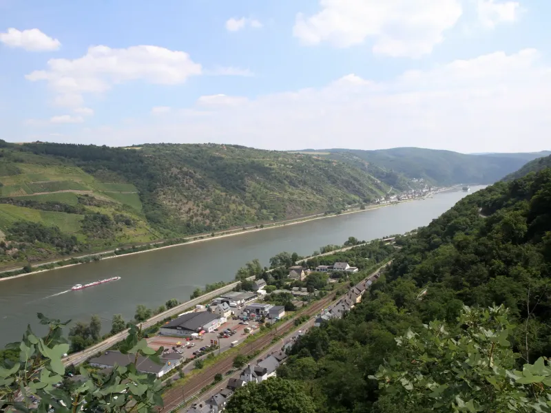 The Rhine curving between steep vineyard slopes near Oberwesel, with a barge on the water and a railway along the bank.
