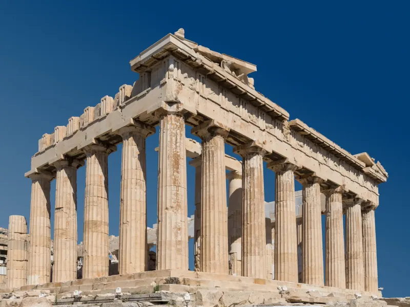 The Doric columns and pediment of the east front of the Parthenon on the Acropolis of Athens against a deep blue sky.