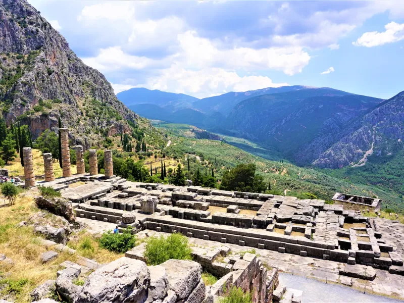 Standing columns of the Temple of Apollo above the terraced sanctuary at Delphi, with the olive valley and Parnassus beyond.
