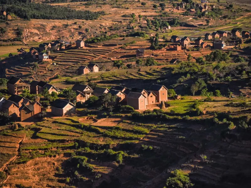 Low sunlight across a terraced valley and a cluster of village houses in the Malagasy highlands.