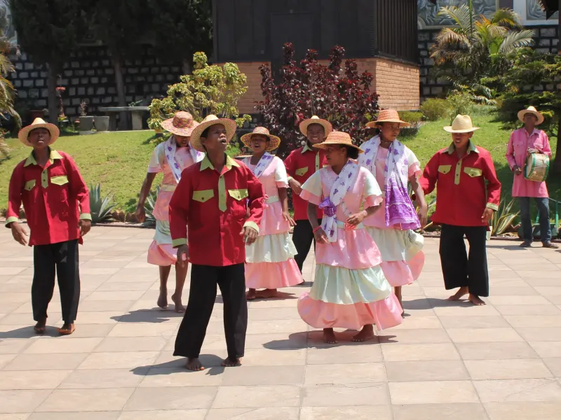 A hiragasy troupe in red jackets and pink dresses performing on a paved square at Ambositra in the central highlands.