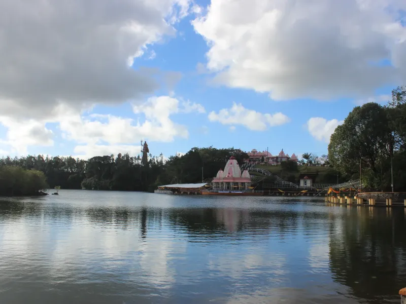 Temples and a tall standing statue reflected in the water of Ganga Talao, the sacred crater lake in the uplands of Mauritius.