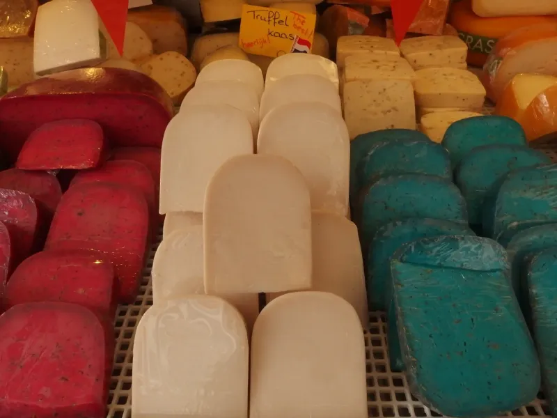 Wheels and blocks of Dutch cheese stacked on a market stall in red, green and plain yellow wax.