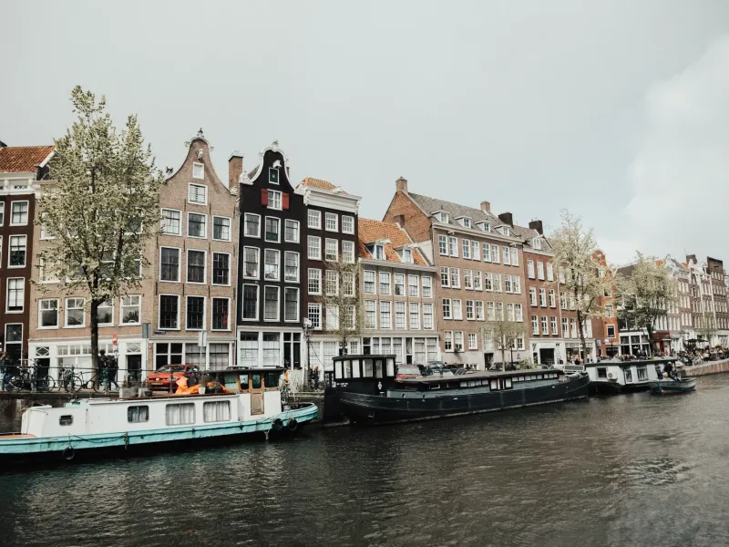 A row of narrow seventeenth-century canal houses with stepped and bell gables above moored barges on an Amsterdam canal.