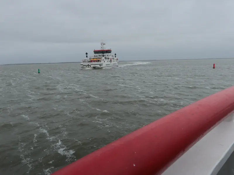 The shallow gray water of the Dutch Wadden Sea from the deck of the Ameland ferry, a second ferry crossing in the distance.