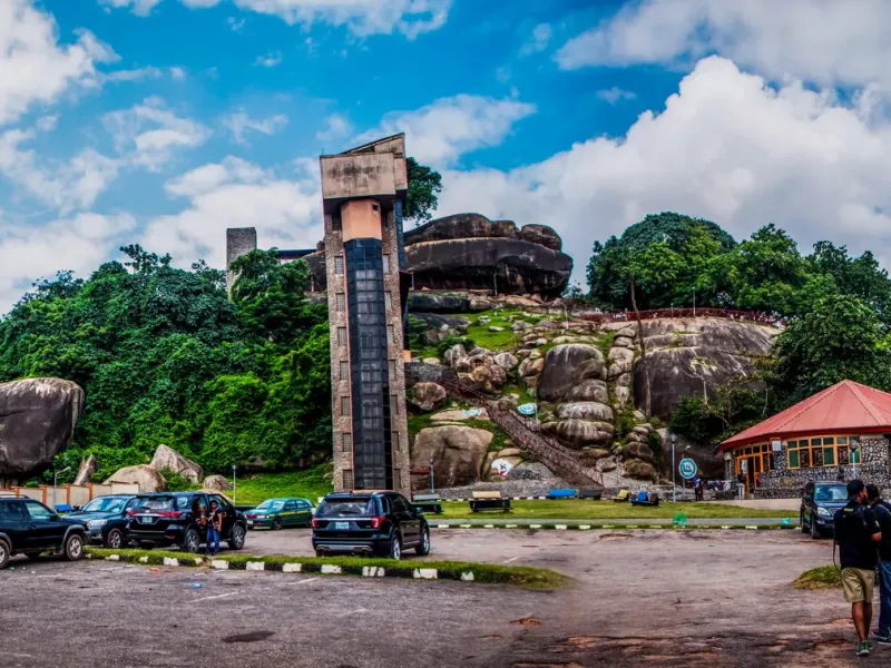 Visitors and a tour coach at the foot of Olumo Rock in Abeokuta, Ogun State, the visitor lift tower on the outcrop.