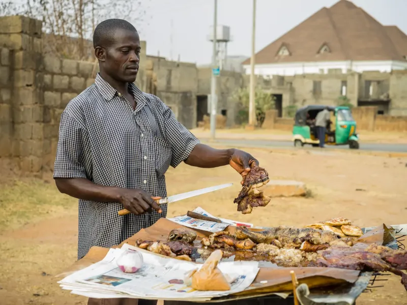 A vendor slicing suya from skewers at a roadside stall in the Asokoro district of Abuja, Nigeria.
