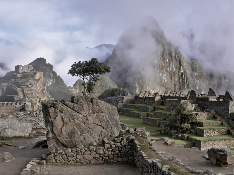 The stone terraces and walls of Machu Picchu in Peru emerging from mist, the peak behind half hidden in cloud