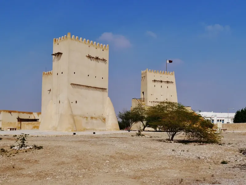 Two pale watchtowers with crenellated tops standing above a low stone wall at Umm Salal Mohammed