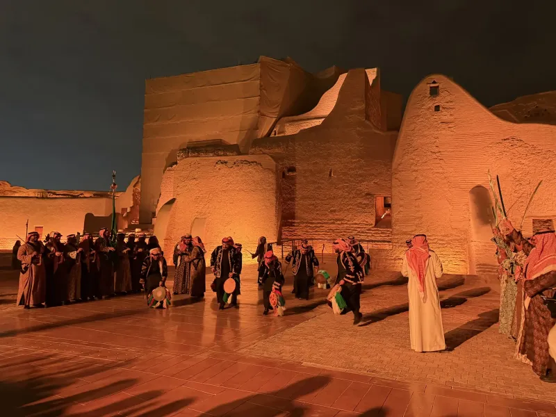 Performers in traditional dress for the Najdi ardha sword dance against the floodlit mud-brick walls of At-Turaif, Diriyah.