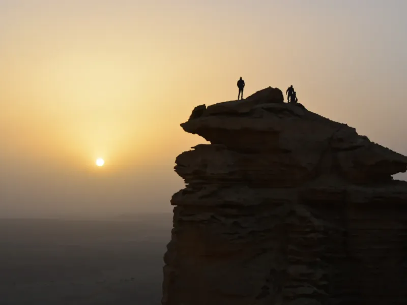 Walkers silhouetted on the Jebel Fihrayn escarpment north-west of Riyadh, Saudi Arabia, as the sun sets over the plain below.