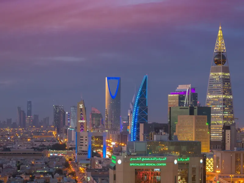 The towers of central Riyadh at dusk, with the Kingdom Centre and Al Faisaliah lit against a violet sky.