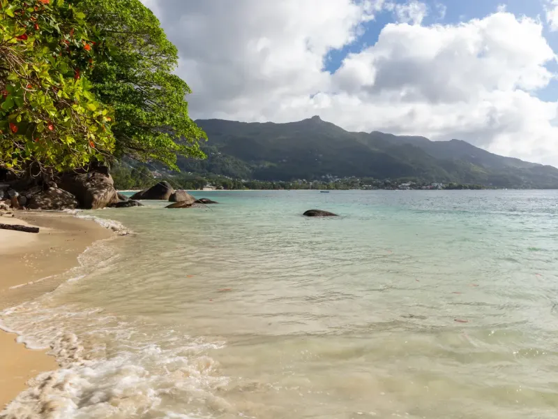 The long sand of Beau Vallon bay on Mahé, calm water and the island's mountain ridge behind.