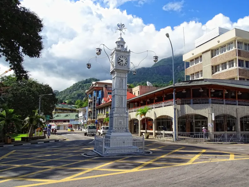 The silver clock tower at the central junction of Victoria on Mahé, colonial-era buildings and wooded hills behind.