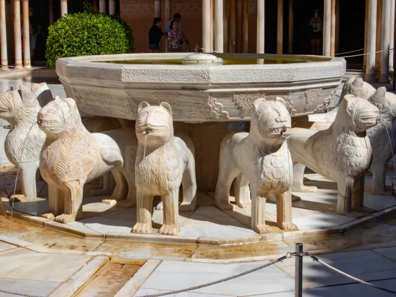 Carved marble lions spouting water beneath the inscribed basin of the lion fountain in the Alhambra at Granada, Spain.