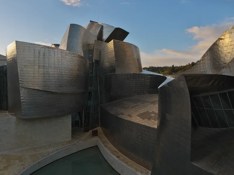 The curved titanium and limestone volumes of the Guggenheim Museum in Bilbao, Spain, in low afternoon sun.