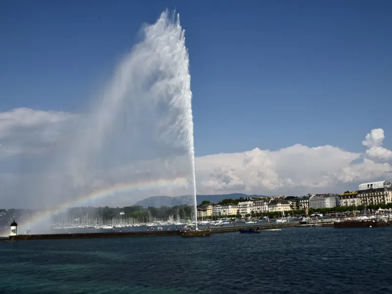 The Jet d'Eau throwing a tall plume of water above Lake Geneva at Geneva, a rainbow forming in the spray.