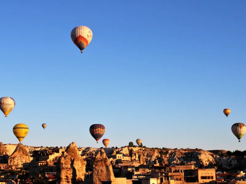 Hot air balloons rising over the rock cones and carved valleys of Goreme in Cappadocia, Turkey, in early morning light.