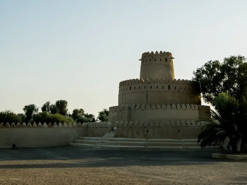 The round crenellated tower and outer wall of Al Jahili Fort in Al Ain, with palms alongside