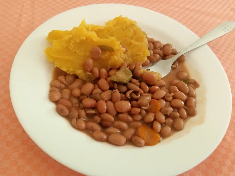 A plate of mashed green banana with beans and a fork, a everyday Ugandan meal.