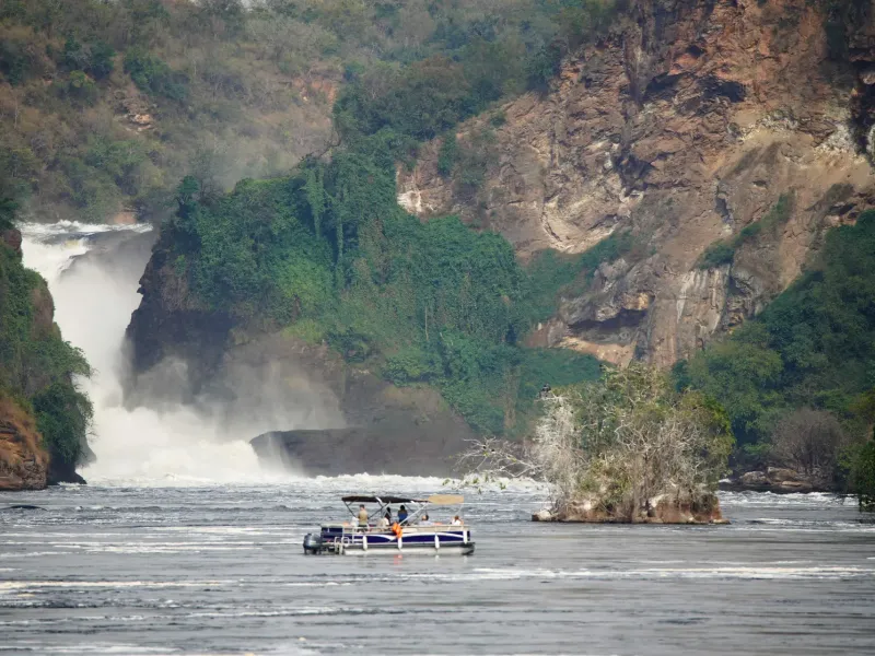 The Nile forcing through a narrow rock gorge at Murchison Falls in Uganda, throwing spray, a small launch below.