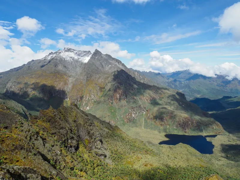 A snow and ice capped peak rising above moorland and a dark tarn in the Rwenzori Mountains, Uganda.