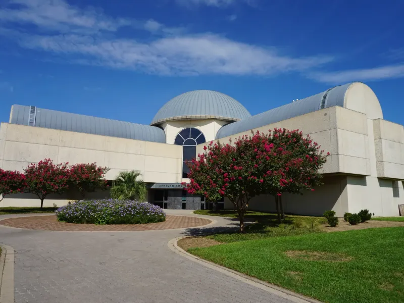 The domed building of the African American Museum at Fair Park in Dallas framed by flowering crape myrtles.