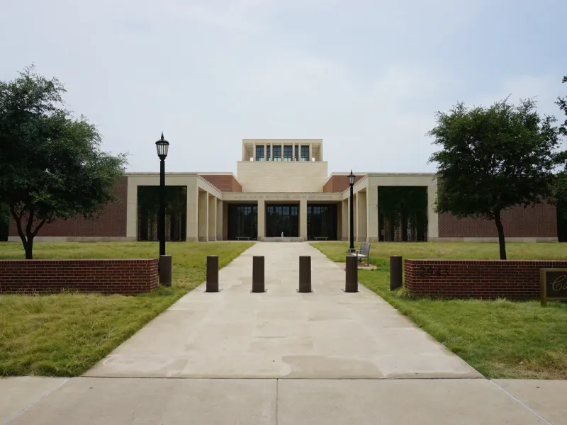 A walkway lined with lawns and lamps leading to the limestone entrance of the George W. Bush Presidential Center.