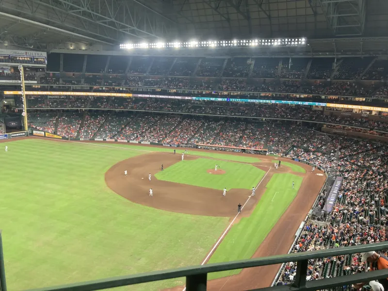 A baseball game in progress under the closed roof of a packed downtown Houston ballpark, seen from the upper deck.