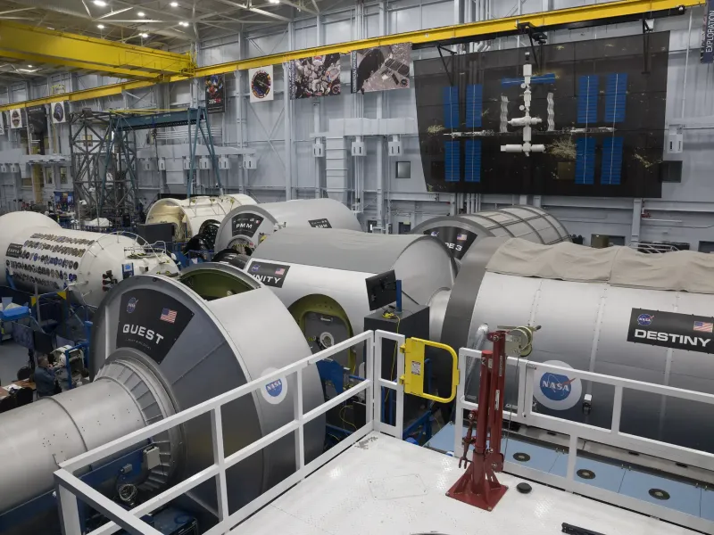 Full size International Space Station training modules marked with NASA logos inside a large hangar in Houston.