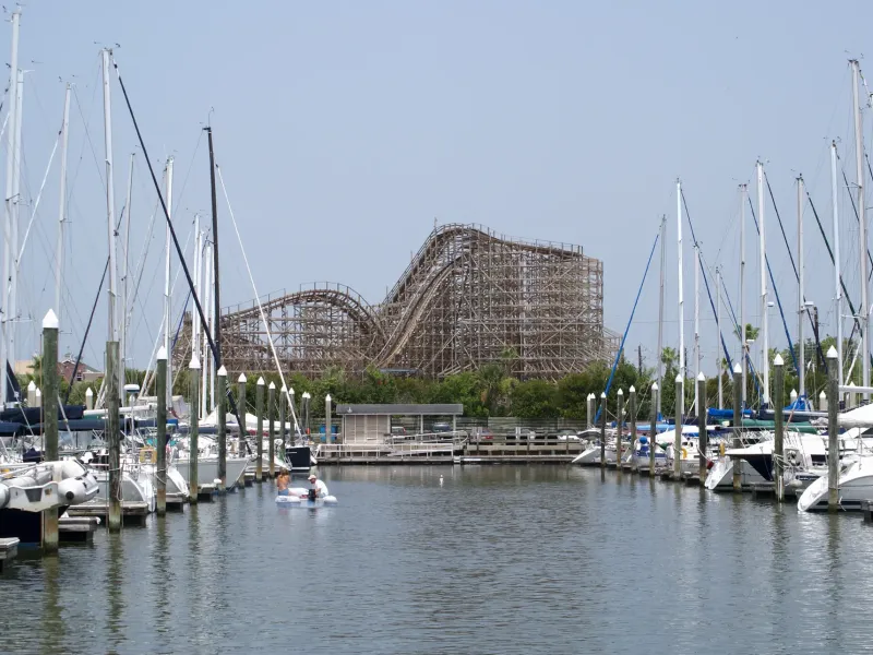 Sailboats moored in a marina with the wooden Boardwalk Bullet roller coaster beyond at the Kemah Boardwalk.