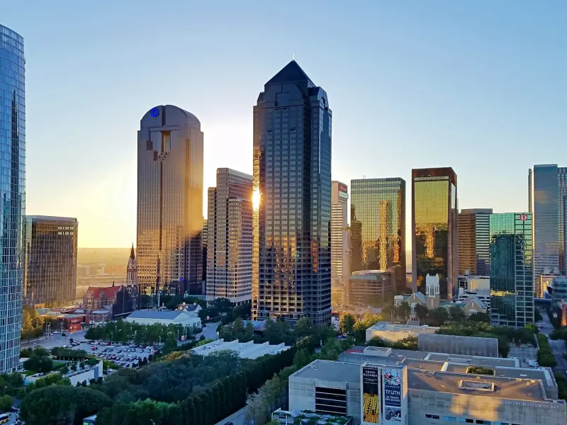 Glass towers of downtown Dallas catch the late sun above the trees and museums of the Dallas Arts District.