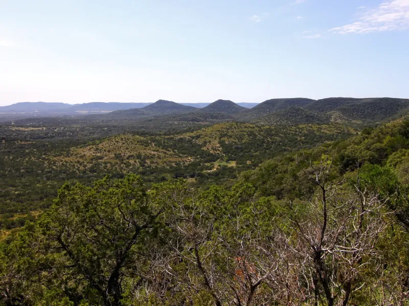 Wooded hills and limestone ridges stretching to the horizon, seen from an overlook in the Texas Hill Country.