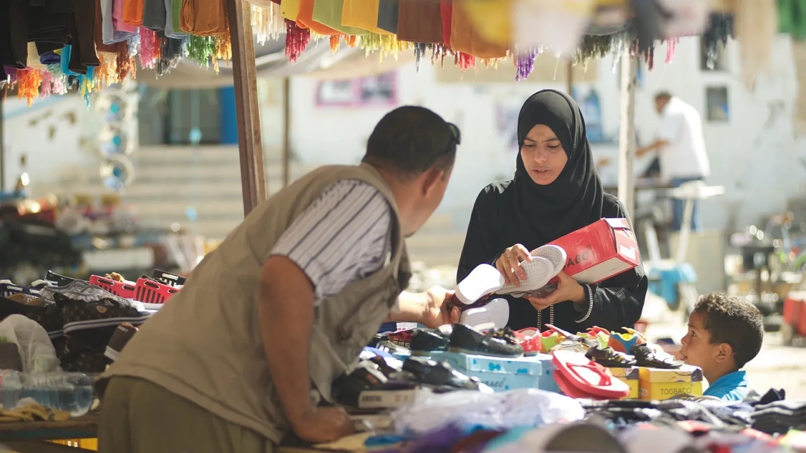 A woman in a black hijab holds up a pair of white sandals
