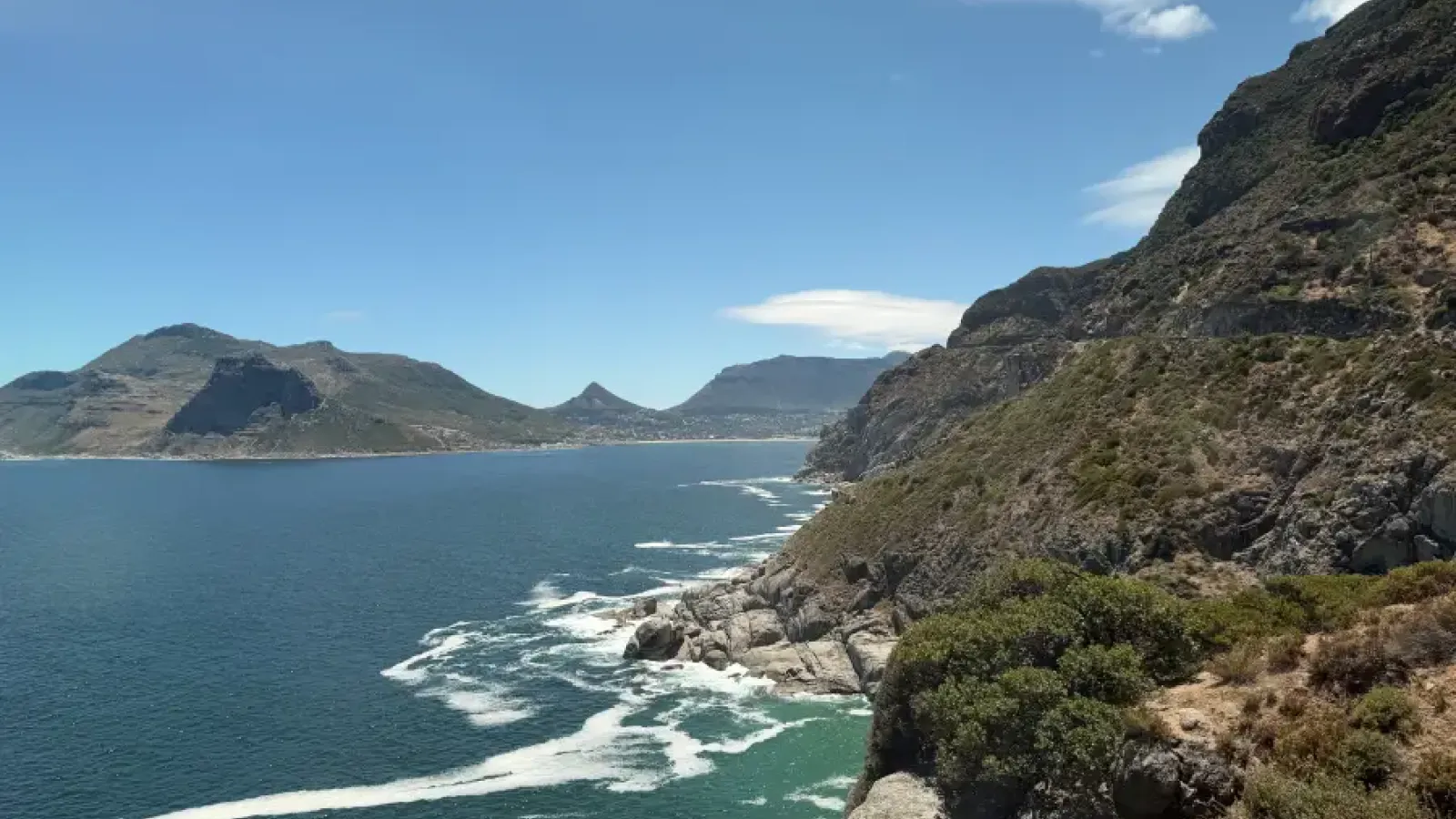 Dramatic rocky cliffs overlooking Hout Bay's turquoise waters with mountain backdrop; captured for eat-mea-2026 travel sho