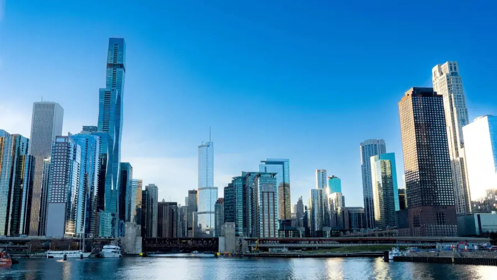 Chicago downtown skyline with glass skyscrapers reflecting over the Chicago River on a clear blue-sky day.