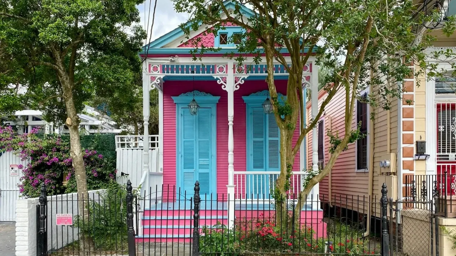 A brightly painted pink and blue Creole cottage with ornate gingerbread trim and a picket fence in a historic New Orleans neighborhood