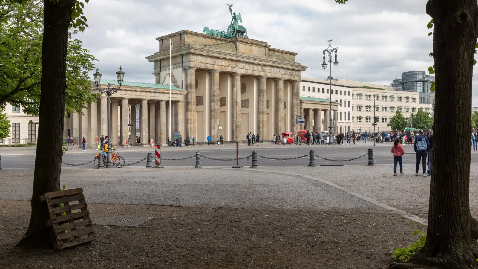 The Brandenburg Gate seen down the Pariser Platz between two plane trees, with the quadriga on top against a gray sky.