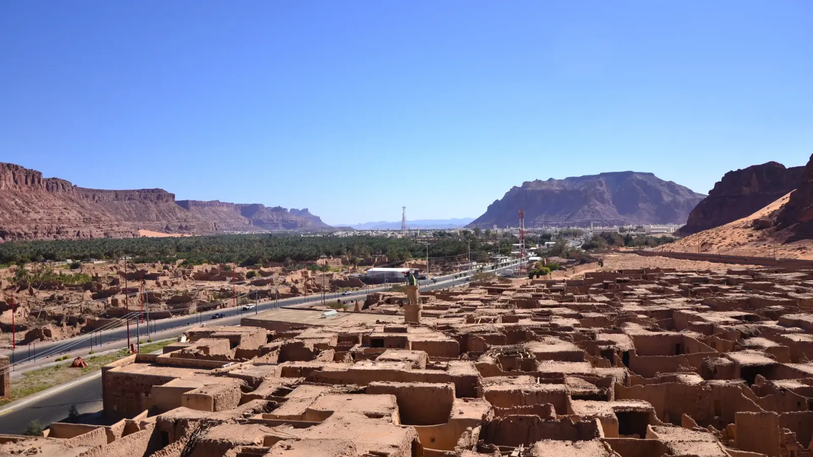 The AlUla valley in north-west Saudi Arabia, its ruined mud-brick town in front and sandstone cliffs closing the horizon.