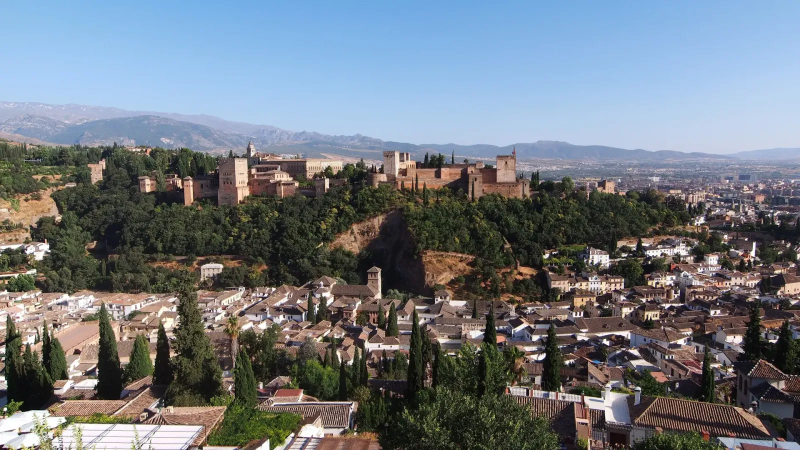The red towers and palaces of the Alhambra on their wooded ridge above the white houses of the Albaicin in Granada, Spain.