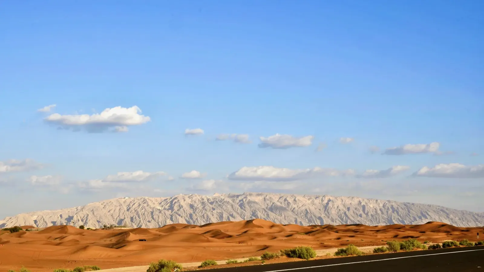 Red dunes in the foreground with the long limestone ridge of Jebel Hafit rising behind