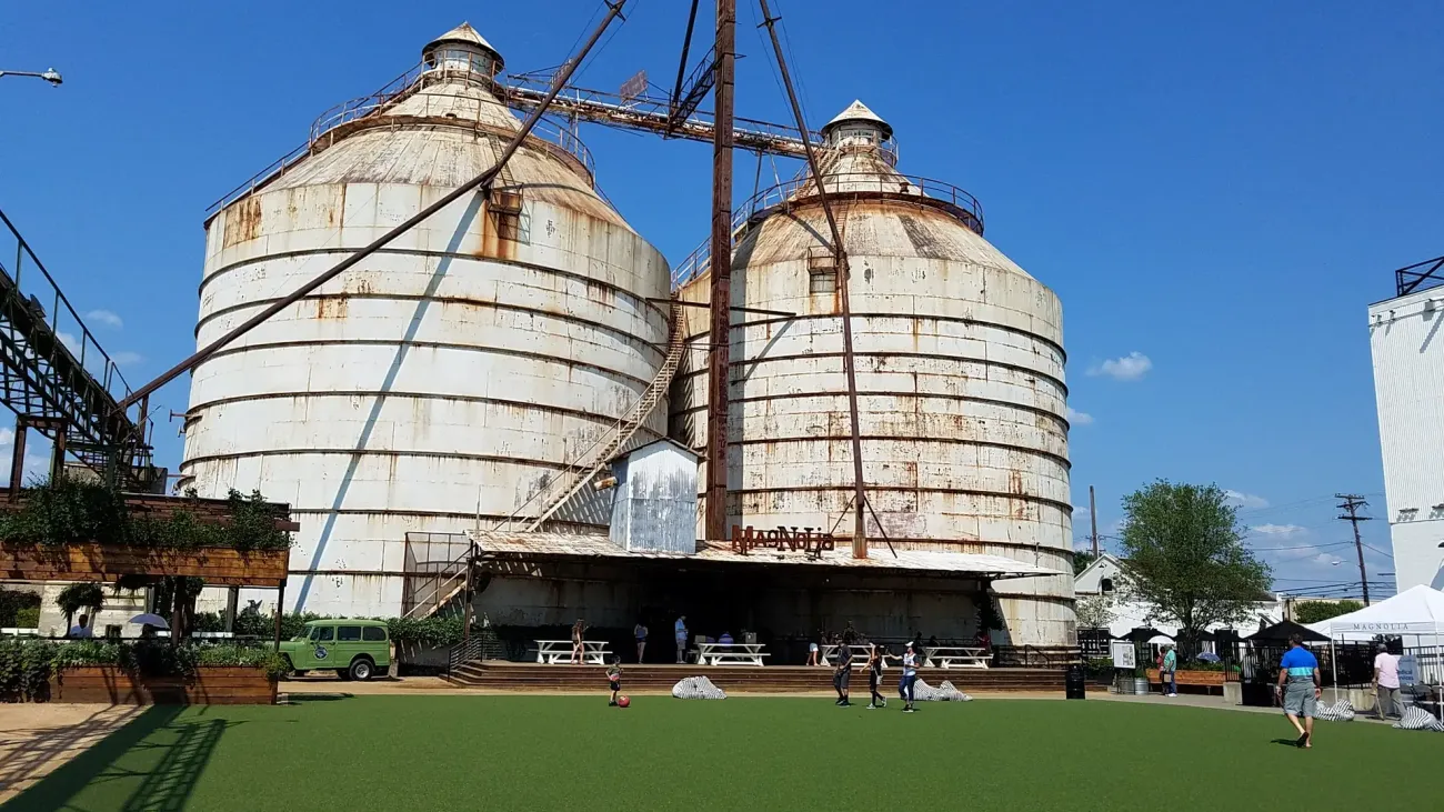 Two weathered steel grain silos rising over a lawn and market stalls at Magnolia Market in Waco.