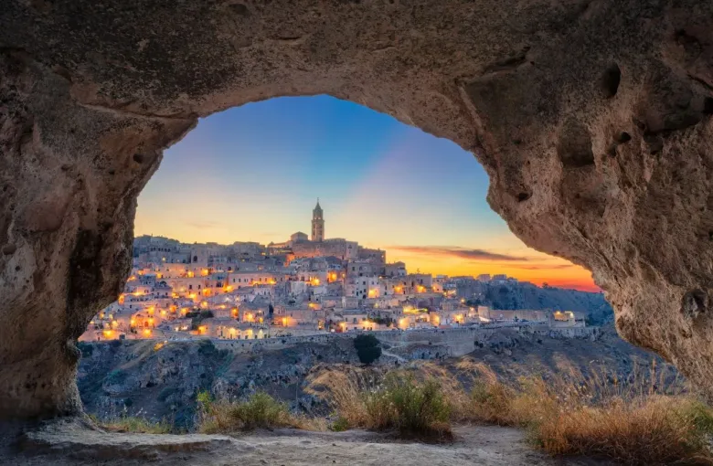 The stone houses of the Matera sassi at dusk, framed by the mouth of a cave