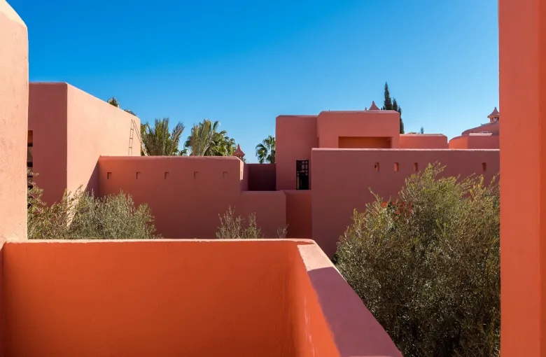 Salmon pink rendered terraces and stairways with palm trees against a clear blue sky.