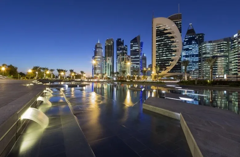 The Doha skyline at dusk, its towers reflected in the water of the bay.