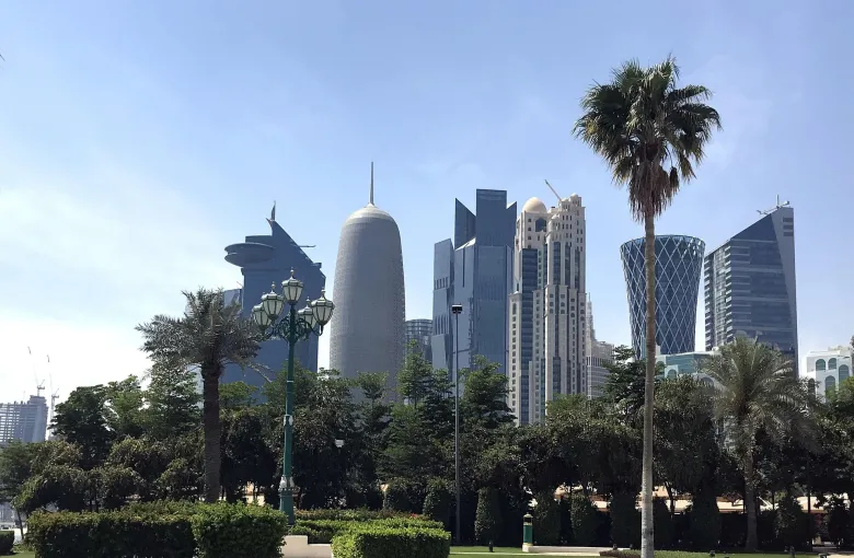 The West Bay skyline of Doha rising behind palm trees and parkland.