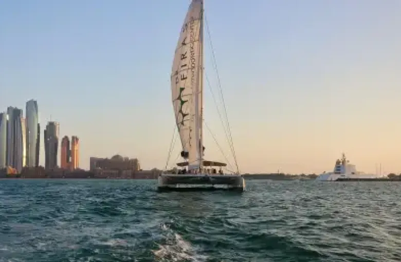 A sailing catamaran on the water off the Dubai coast at dusk.