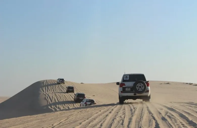 Four-wheel-drive vehicles crossing sand dunes in the Qatari desert.