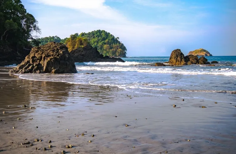 Surf breaking on a rocky Costa Rican beach below a forested headland.
